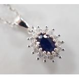 A modern 9ct white gold, sapphire and diamond set oval cluster pendant, overall 15mm,on a modern 9ct