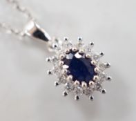 A modern 9ct white gold, sapphire and diamond set oval cluster pendant, overall 15mm,on a modern 9ct