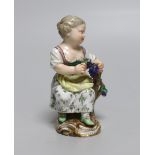 An early 19th century Meissen figure of a girl seated on a tree stump holding a bunch of grapes,