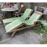 A pair of weathered teak garden loungers with seat cushions and rain covers