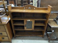 An Art Nouveau oak open bookcase, fitted with a central cupboard, the door inset with a hammered