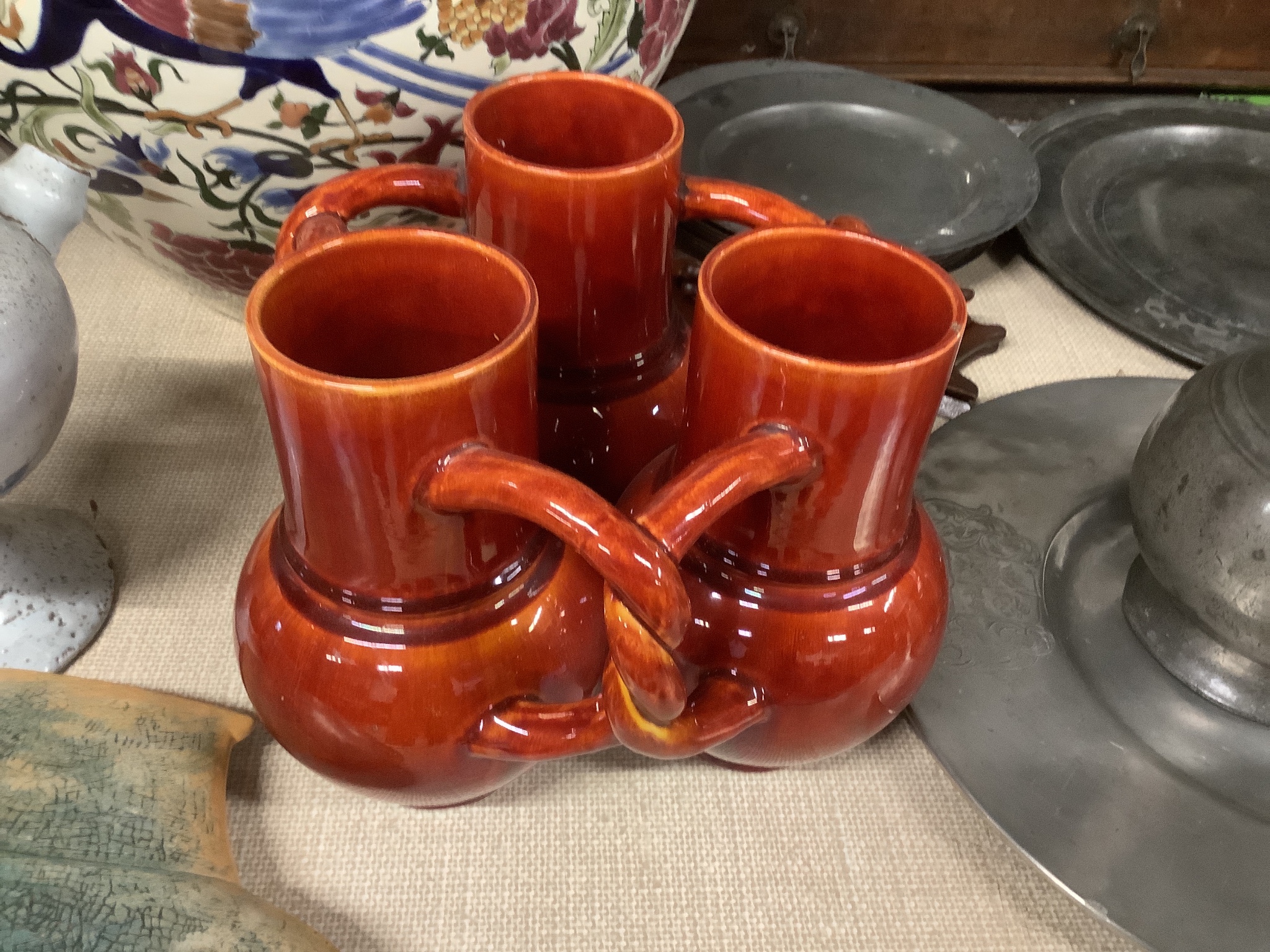 A Burmantofts Pottery three section fuddling cup with interwoven handles in dark burnt orange,
