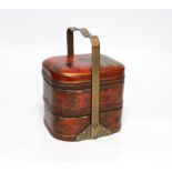 A Japanese red lacquered two section container with brass handle, 21cm high