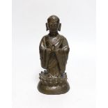 A Chinese bronze figure of a luohan, late Ming dynasty, on lotus design base, 21cm high