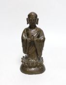 A Chinese bronze figure of a luohan, late Ming dynasty, on lotus design base, 21cm high