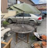 A circular weathered teak garden table, diameter 122cm, height 75cm parasol and bench