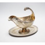 A continental white metal sauceboat on stand, with flying scroll leopard's head handle, length 23.