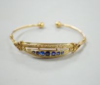 A 750 yellow metal and graduated seven stone sapphire?, paste and doublet set open work bangle,