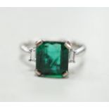 A modern 18k white metal and single stone emerald set ring, baguette cut diamond set shoulders, size