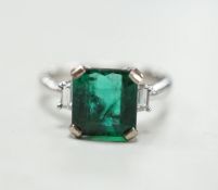 A modern 18k white metal and single stone emerald set ring, baguette cut diamond set shoulders, size