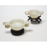 Two Chinese pale celadon jade cups, Qing dynasty, on carved hardwood stands, largest 13cm wide