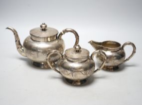 CITES- A Chinese engraved white metal three piece tea set, decorated with birds amongst foliage,