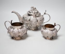 An Indian embossed white metal three piece tea set, with cobra handles and elephant finial, 25.