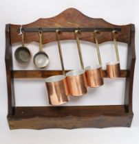 Two small copper sauce pans, four graduated copper measuring pans and a hanging rack, largest 47cm