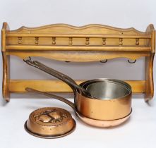 Three copper saucepans, a frying pan, a decorative mould and a pine hanging rack, largest 58cm wide