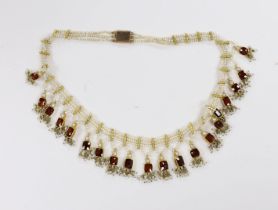 An Indian yellow metal mounted triple strand seed pearl and graduated twenty stone garnet set drop