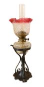 A late Victorian wrought iron and cut glass oil lamp with cranberry tinted glass shade, overall