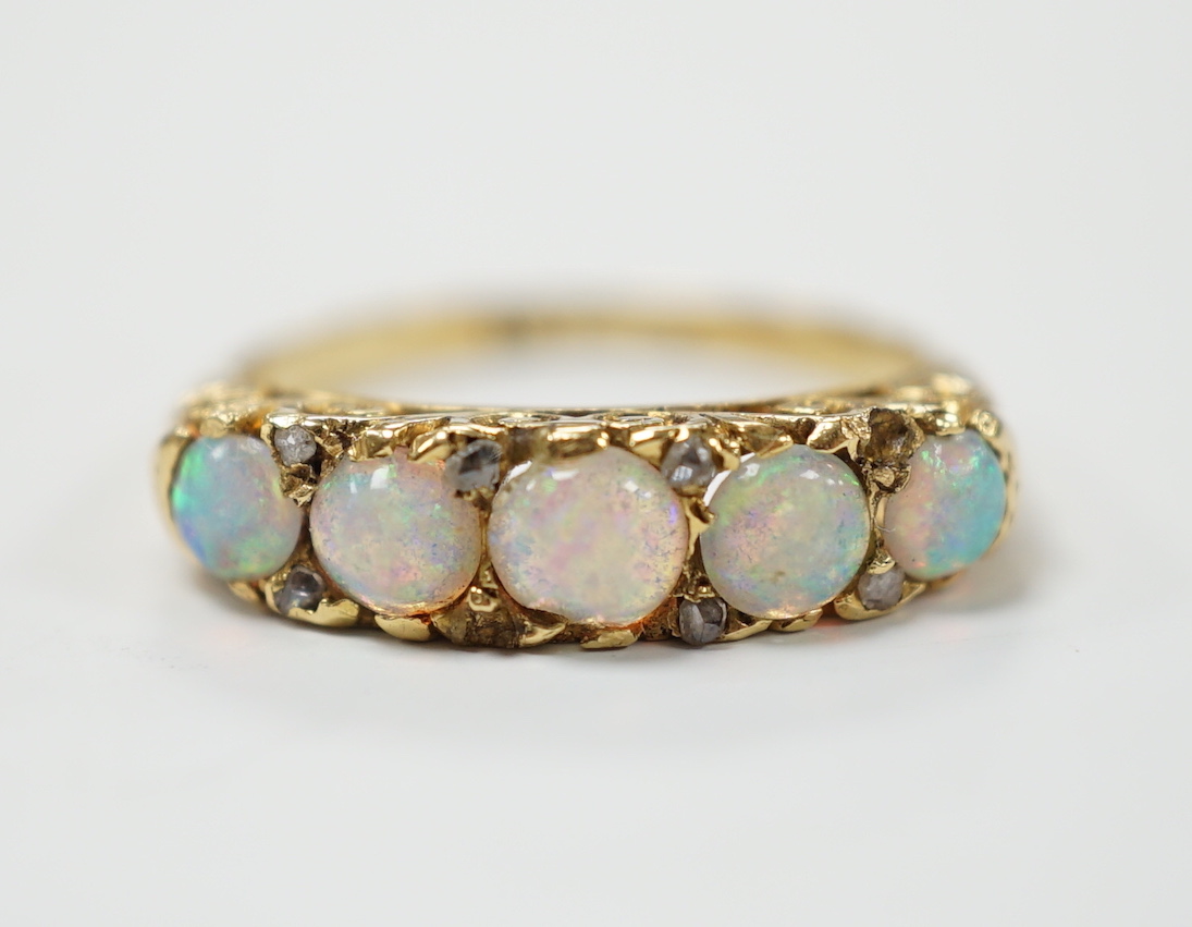 A late Victorian yellow metal and white opal five stone ring with diamond chip set spacers, size M