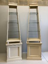 David Hicks - a pair of cream painted obelisk open shelved cabinets, on square plinths, designed