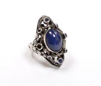 An Arts & Crafts pierced white metal and blue cabochon set dress ring, bordered with seven (ex 8)