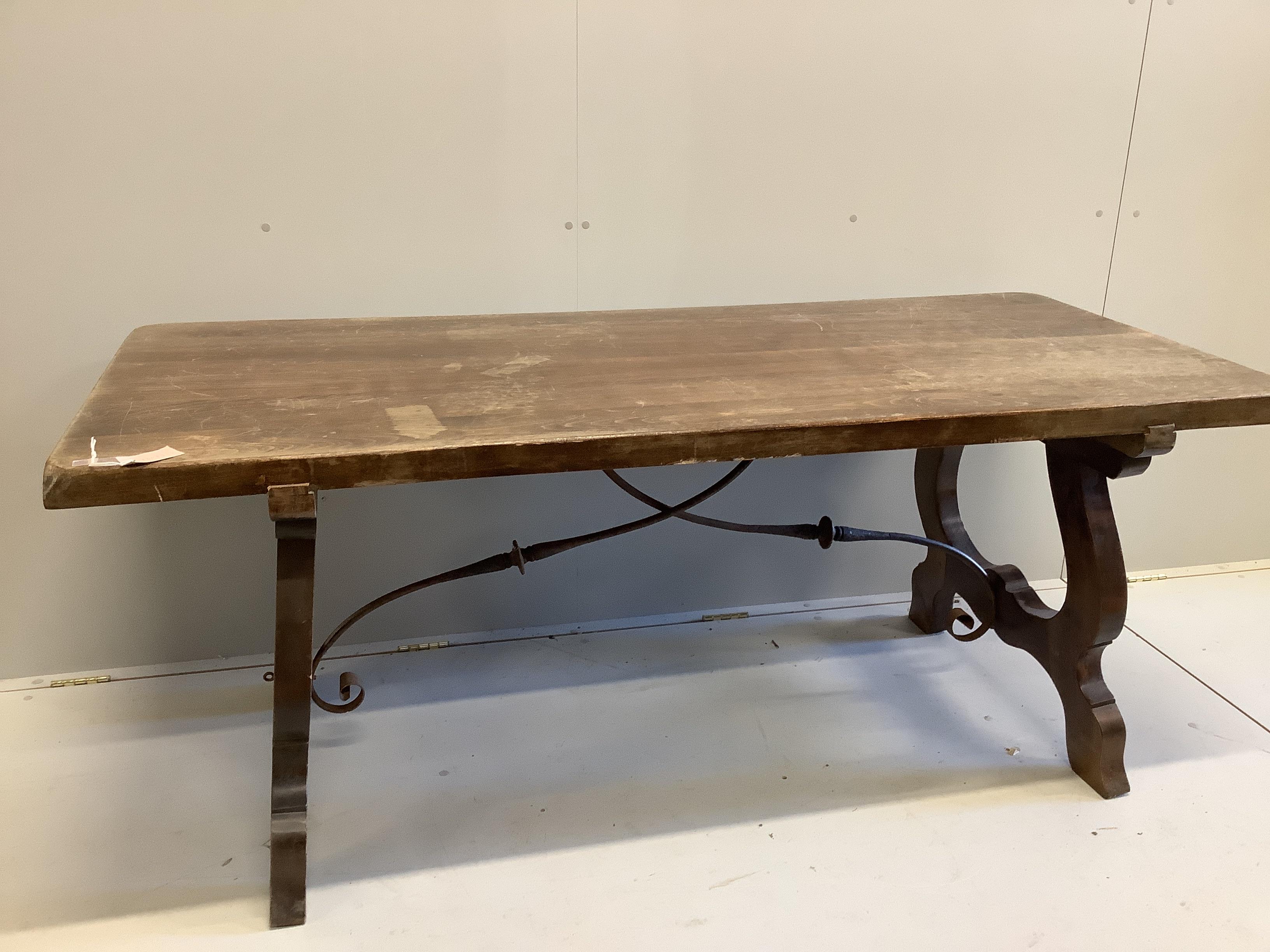 A Spanish style beech rectangular dining table, on shaped supports with iron stretcher, length