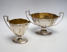 A George III engraved silver two handled oval pedestal sugar bowl and matching cream jug, Henry