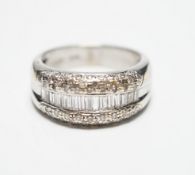 A modern 750 white metal and graduated baguette cut diamond set half hoop ring, with diamond chip