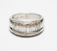 A modern 750 white metal and graduated baguette cut diamond set half hoop ring, with diamond chip