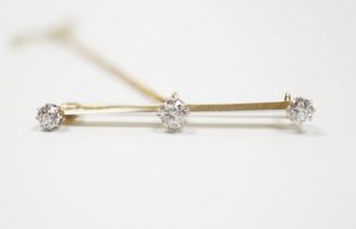 A yellow metal and three stone diamond set bar brooch, 37mm, with safety chain, gross weight 3