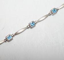 A modern brushed 9ct white gold and seven stone square cut blue topaz? set bracelet, 18cm, gross