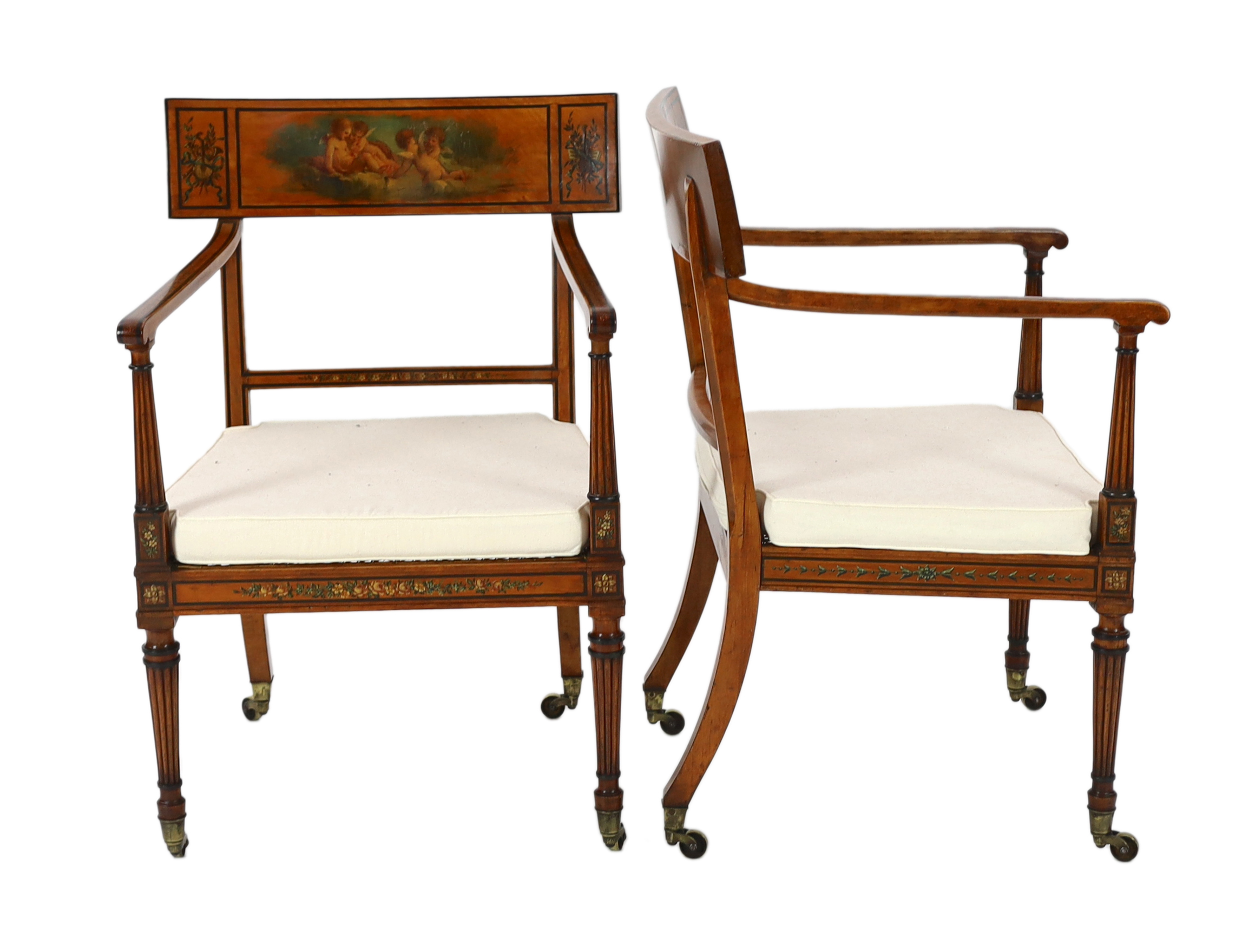 A pair of Edwardian Sheraton revival painted satinwood elbow chairs, decorated with cherubs, flowers