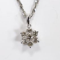 A modern 18k white metal and seven stone diamond cluster set flower head pendant, overall 15mm, on a