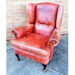 A RED LEATHER UPHOSLTERED WING ARMCHAIR with scroll arms, on cabriole supports, 86cm wide