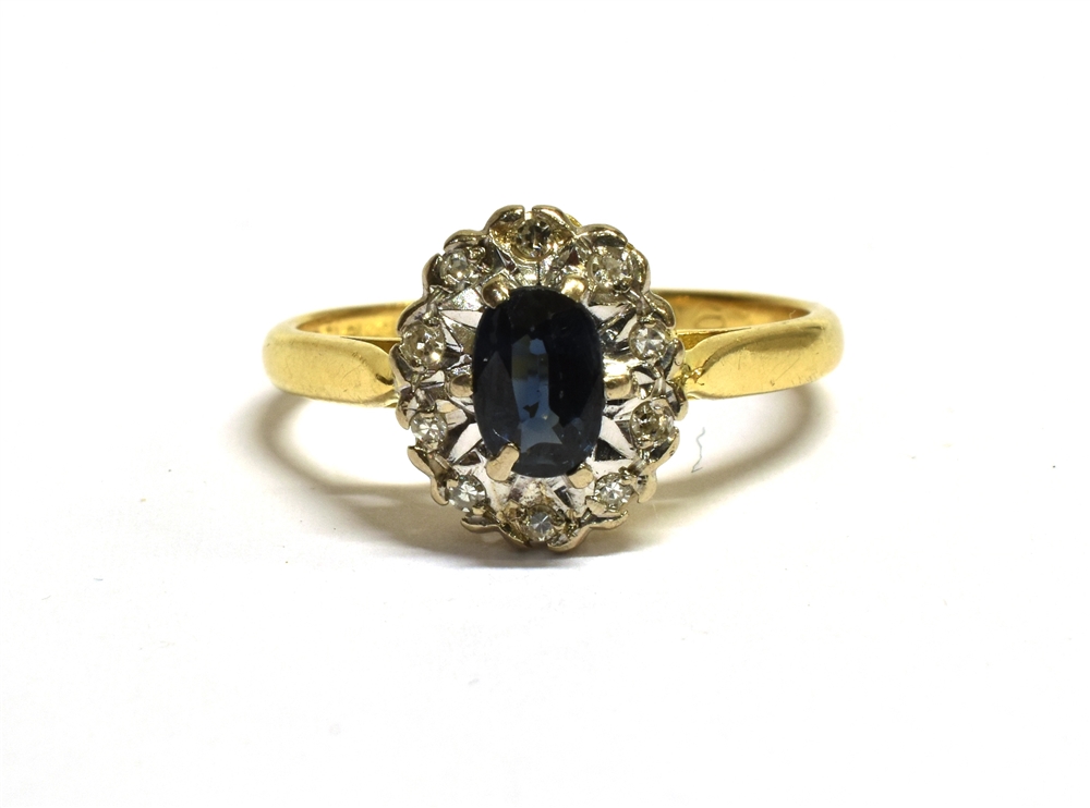 18CT GOLD SAPPHIRE CLUSTER RING The cluster measuring 1.1 x 0.9cm and set with a central oval blue