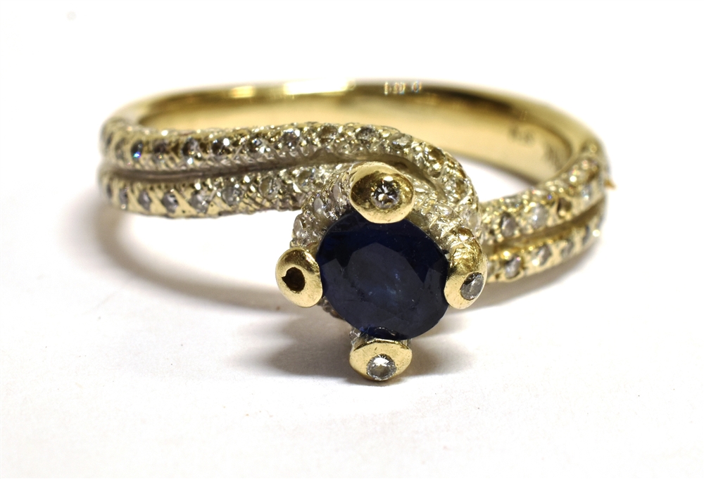 A STAMPED 18K SAPPHIRE AND DIAMOND CROSS OVER RING The ring in white metal and centrally set with