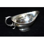 A WHITE METAL SAUCE BOAT The boat with beaded rim border and scroll handle, some faded markings,