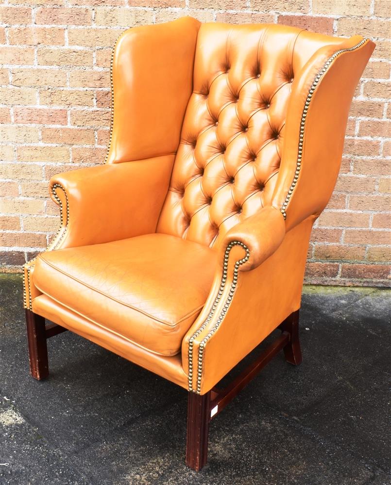 A TAN LEATHER BUTTON UPHOLSTERED WING ARMCHAIR with scroll arms, on square moulded supports, 78cm