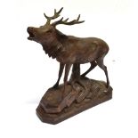 A BLACK FOREST CARVED WOODEN FIGURE OF A STAG Standing on a rocky outcrop against a tree trunk,