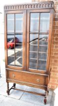 A GLAZED OAK BOOKCASE with four adjustable shelves, drawer to base on barley twist supports, 85cm