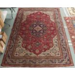 A red ground Tabriz rug with dark blue central medallion, cream spandrels and dark blue borders,
