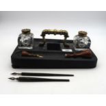 An ebonised desk stand, with cast brass handle and heavy glass inkwells; accompanying calligrapher's