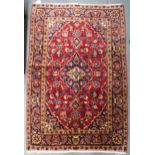 A red ground Kashan rug with blue central medallion, matching spandrels and blue flower head border,