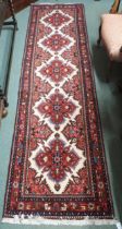 A cream ground Hamadan runner with five red flower head medallions, pink spandrels and multicoloured