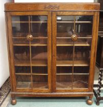 A 20th century oak two door glazed bookcase with pair of glazed doors turned ball supports, 129cm