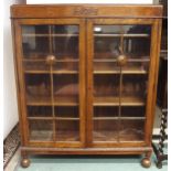 A 20th century oak two door glazed bookcase with pair of glazed doors turned ball supports, 129cm