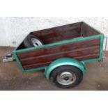 A wood panelled side single axle car trailer with hinged tailgate with mounted lights and spare