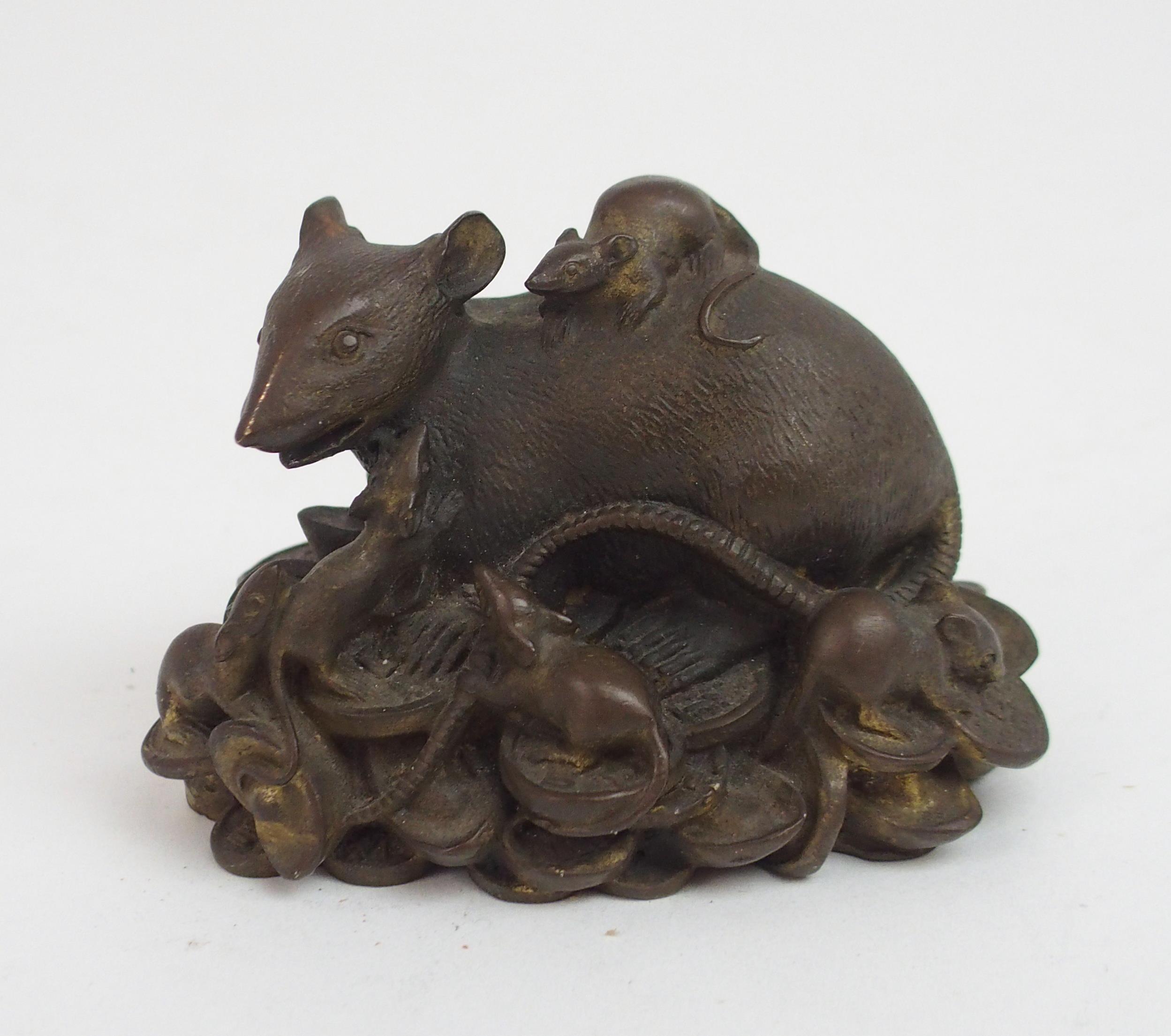 A CHINESE BRONZE FIGURE OF A RECUMBENT RAT modelled seated on a pile of archaic coins, surrounded by