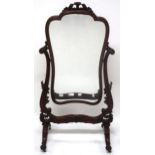 A VICTORIAN MAHOGANY FRAMED CHEVAL DRESSING MIRROR with shaped mirror on scrolled foliate carved