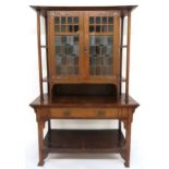 AN OAK ARTS & CRAFTS BOOKCASE with shaped cornice over pair of central leaded stained glass doors