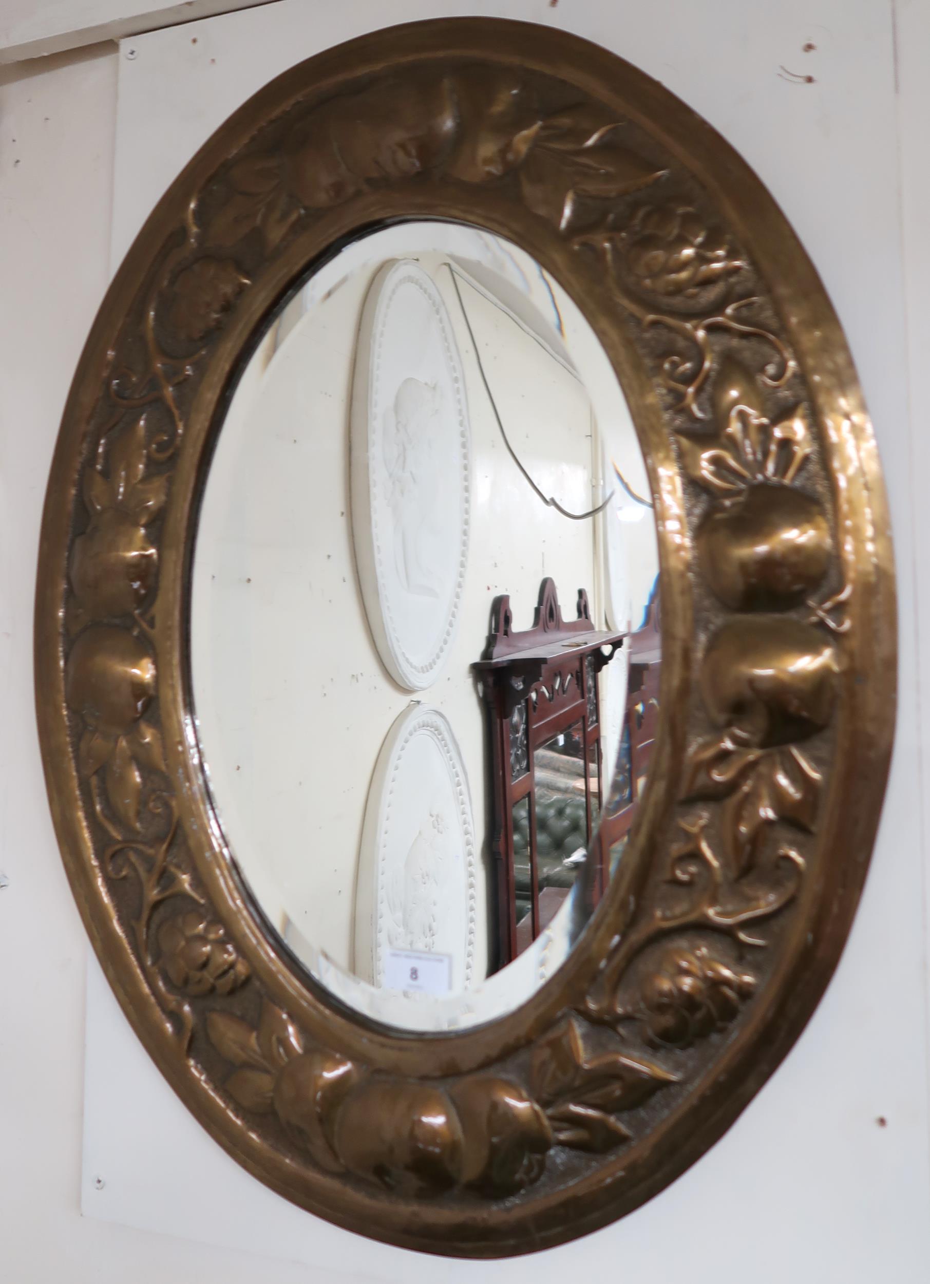 An early 20th century oval brass framed bevelled glass wall mirror with embossed fruit on the vine